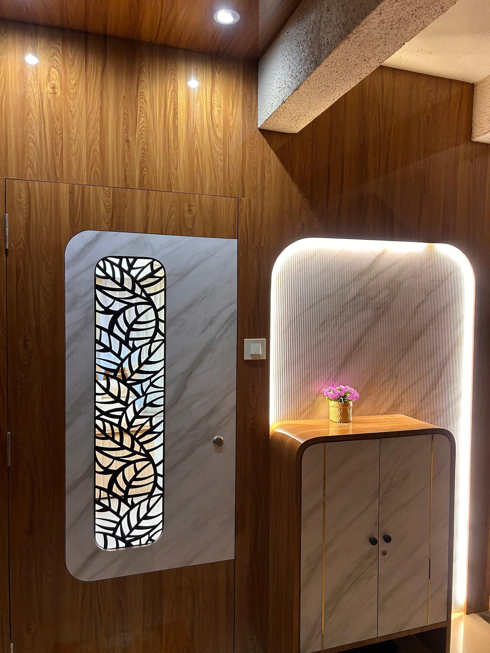 Foyer with teak panelling, a jali-inlay door panel and a backlit mirror above a console